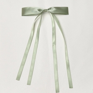Detail of sage green satin hair clip with long ribbons on white leather surface