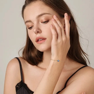 Detalle de una pulsera de cadena dorada con cuenta de ojo turco azul en la muñeca de modelo