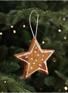 Close-up of a gingerbread-style star ornament with white frosting on a green pine branch