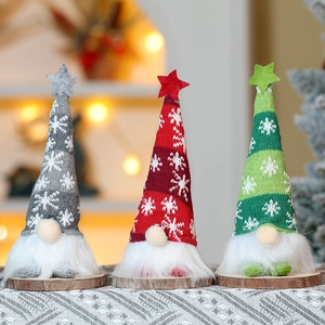 Three glowing knit Christmas gnomes with wooden bases set against warm bokeh lights