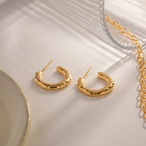 Detail of golden stainless steel C-shaped earrings with hammered texture on a ceramic plate