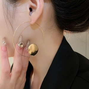 Close-up of minimalist gold geometric hoop earrings with a solid disc on model