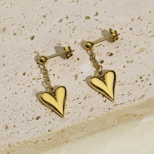 Detail view of gold-plated heart earrings with chain link on a natural stone base