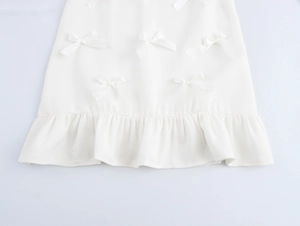 Détail d'une robe blanche ligne A avec tissu texturé, nœud élégant et ourlet à volants