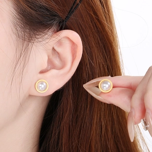 Détail d'une boucle d'oreille en perle blanche avec une base minimaliste en métal doré