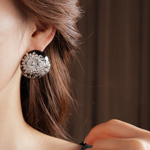 Close-up of vintage large round floral earring with silver sunflower relief on black base
