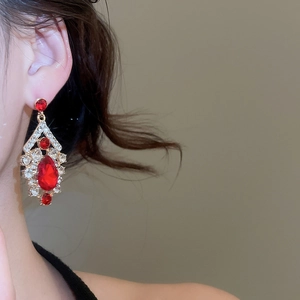 Detailed view of elegant gold drop earrings with red and clear crystals on a model