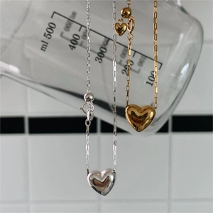 Detail of minimalist 925 silver heart necklaces in gold and silver finish hanging on a beaker