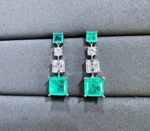 Macro shot of 925 silver emerald cut earrings with dangling green and white gemstones