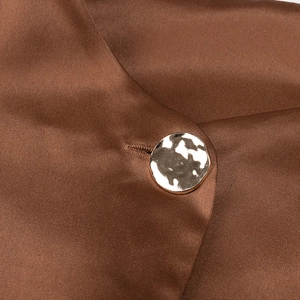 Detailed macro view of the golden hammered button on elegant brown satin fabric