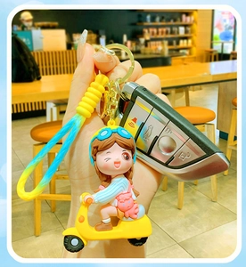 Close-up of cute cartoon girl on scooter keychain with blue and yellow woven strap