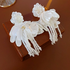 Macro shot of white petal floral earrings with beaded tassel fringe on a leather box