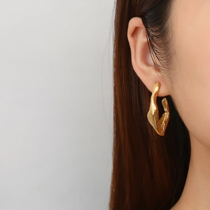 Close-up of golden irregular lava texture C-shape earrings on female model