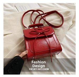 Detail showing the bottom metal studs and bow decoration of the red leather handbag
