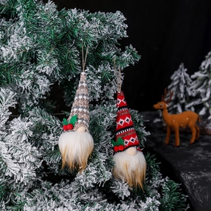 Festive knitted Christmas gnome ornaments with glowing lights hanging on a snowy tree