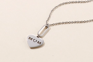 Detail of silver heart necklace with MOM engraving on a minimalist beige surface