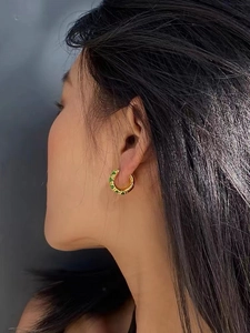 Close-up of gold-plated hoop earrings featuring vintage green zircon on a model