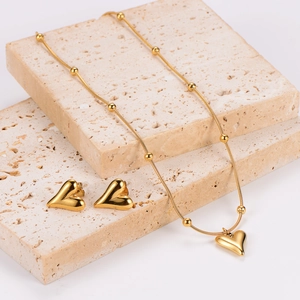 Golden heart necklace and earring jewelry set displayed on elegant beige stones