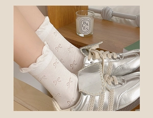 Detailed view of white knit crew socks with bow jacquard patterns and ruffled cuffs
