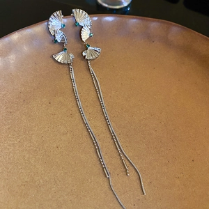 Detail of silver long fringe earrings with fan-shaped green gems on ceramic plate