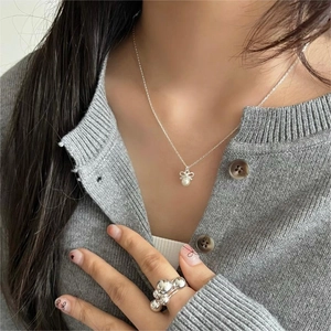 Detail of silver bow pearl necklace and geometric beaded ring worn by a model