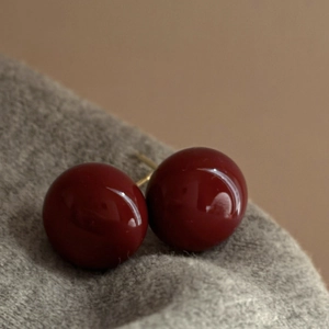 Macro view of dark red pearl stud earrings with gold pins on grey knit fabric texture