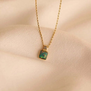 Macro view of a gold square opal pendant showing iridescent green and orange colors