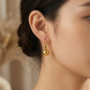 Close-up of elegant gold polished sphere drop earrings worn on a female model's ear