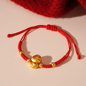 Detail of red braided string bracelet featuring a gold God of Wealth charm and beads