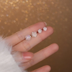 Elegant S925 sterling silver white rose stud earrings held by fingers on golden backdrop
