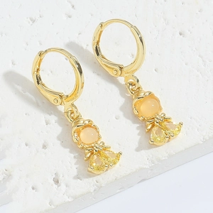 Close-up of golden angel earrings with orange cubic zirconia stones on stone surface