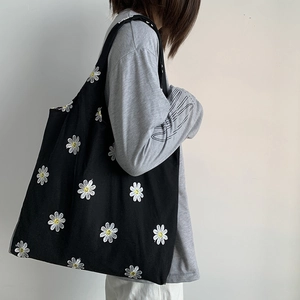 Detailed side view of black canvas tote bag with daisy embroidery on a model