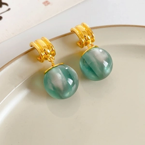 Detail of gold metal earrings with translucent green resin beads on a white plate