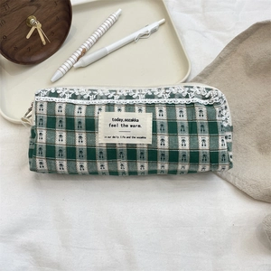 Detail of green plaid canvas pouch with delicate white lace trim and top zipper closure