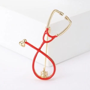 Close-up of a stethoscope brooch with red enamel details and gold-plated metal finish