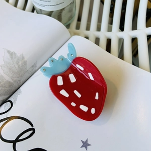 Cute strawberry acetate hair claw clip with rhinestones displayed on an open book