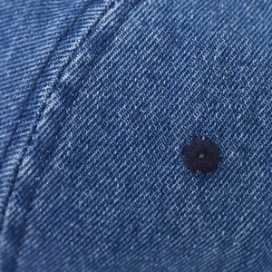 Detailed close-up of blue denim texture and stitched eyelet on a baseball cap