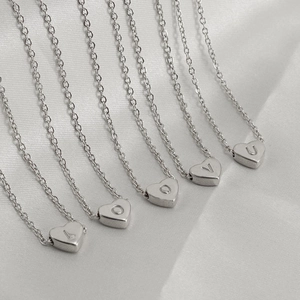 Macro shot of silver heart pendants with engraved letters L, O, V, E on a soft white cloth