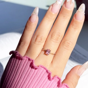 Detail of pink oval gemstone ring with golden chain band on a model's hand