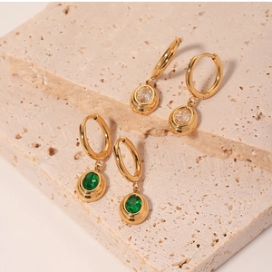 Macro detail of emerald and white zircon charms on golden stainless steel earrings
