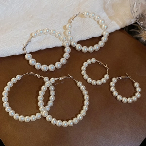 Detailed view of three sizes of elegant white pearl hoop earrings on a textured background