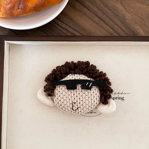 Detail of creative plush character brooch with brown curly hair on a wooden tray