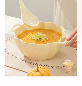 Detail of a ceramic pumpkin soup bowl with handles and a spoon on a cream mat