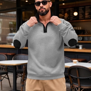 Men's grey half-zip sweatshirt with black elbow patches in a modern outdoor casual setting