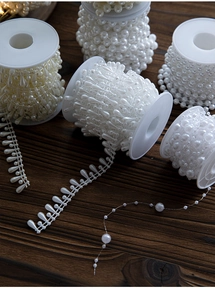 Macro detail of white pearl bead rolls in round and teardrop shapes on wood background
