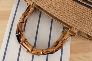Detail of woven straw bag showing bamboo handle with gold hardware and striped texture
