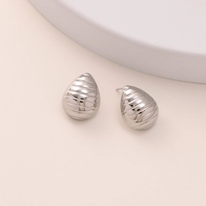 Macro view of silver teardrop earrings with textured horizontal grooves and metallic finish