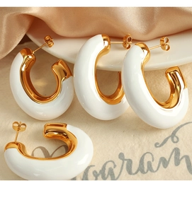 Dettaglio di orecchini a C in smalto bianco e oro su elegante tessuto in seta champagne
