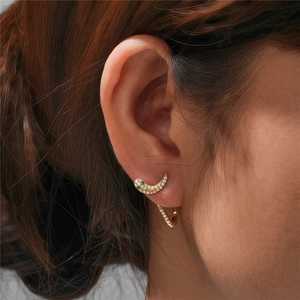 Detail of gold crescent moon and hoop earrings with white and green zircons on a model