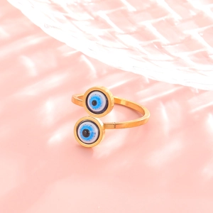 Macro detail of golden evil eye ring showing blue enamel circles on soft pink background